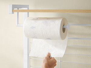 Papierhandtuchhalter zur Wandmontage mit einer Rolle weißer Papierhandtücher. Eine Hand streckt sich aus, um ein Blatt abzureißen