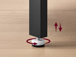 Close-up of a furniture leg adjuster with a red circular base and black stem, showing upward and downward arrow indicators for height adjustment.